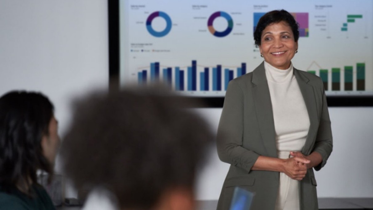 Frau vor einer Präsentation mit Diagrammen, Zuhörer im Vordergrund Frau vor einer Präsentation mit Diagrammen, Zuhörer im Vordergrund