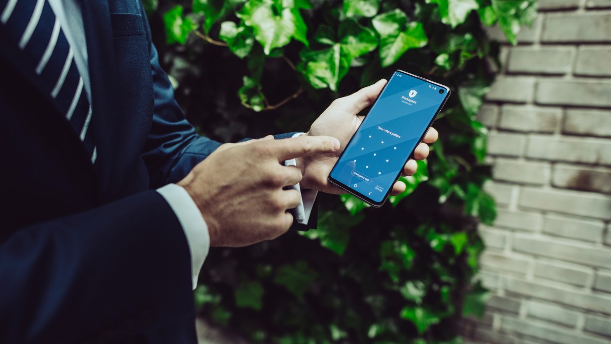 A man in a suit, holding a smartphone with a visible lock screen