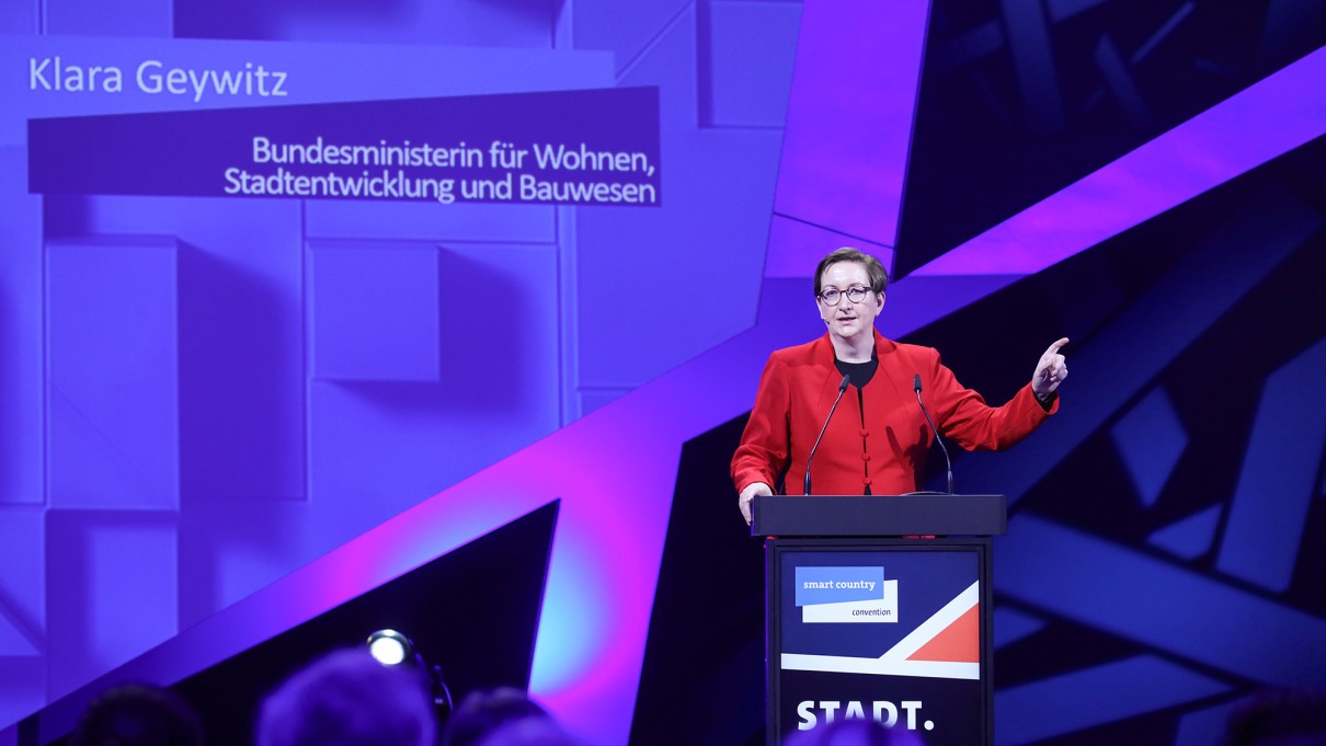 Klara Geywitz, Bundesministerin für Wohnen, Stadtentwicklung und Bauwesen steht auf der SCCON-Bühne hinter einem Rednerpult. Klara Geywitz, Bundesministerin für Wohnen, Stadtentwicklung und Bauwesen steht auf der SCCON-Bühne hinter einem Rednerpult.