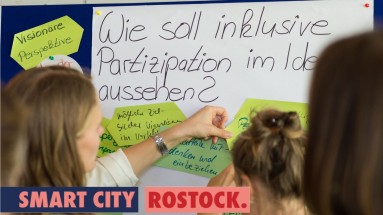 Three women in front of a flipchart with the question 'What should inclusive participation look like?' written on it.