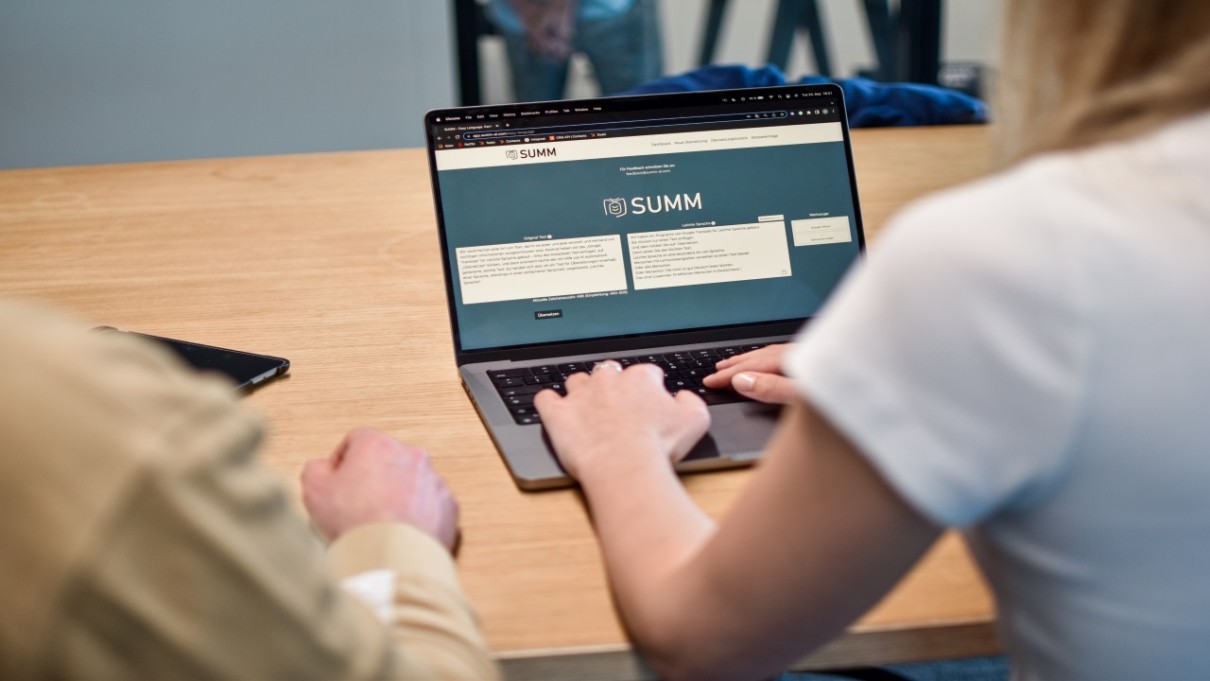 Frau von hinten vor einem Laptop, auf dem Laptop das Tool von SUMM AI Frau von hinten vor einem Laptop, auf dem Laptop das Tool von SUMM AI