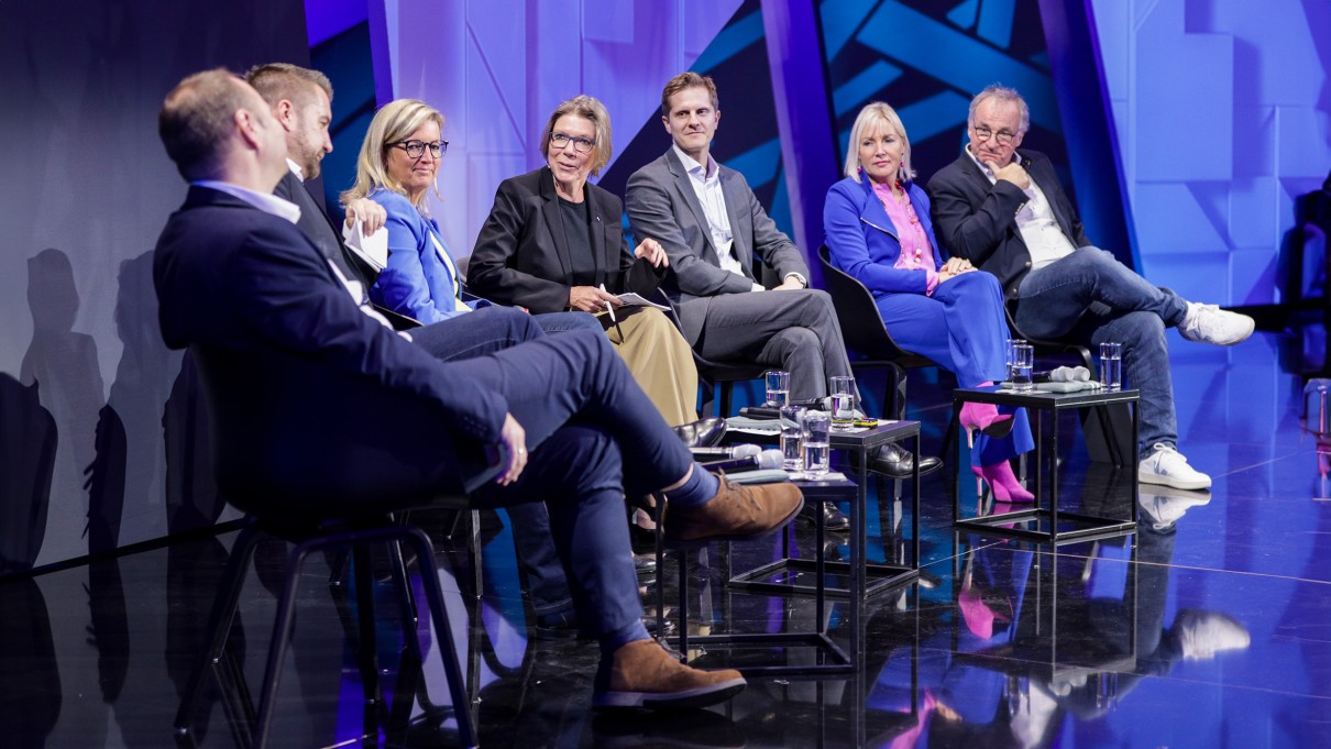 Sechs D16-Panel-Sprecher:Innen und eine Moderatorin sitzen auf der SCCON-Bühne. Sechs D16-Panel-Sprecher:Innen und eine Moderatorin sitzen auf der SCCON-Bühne.