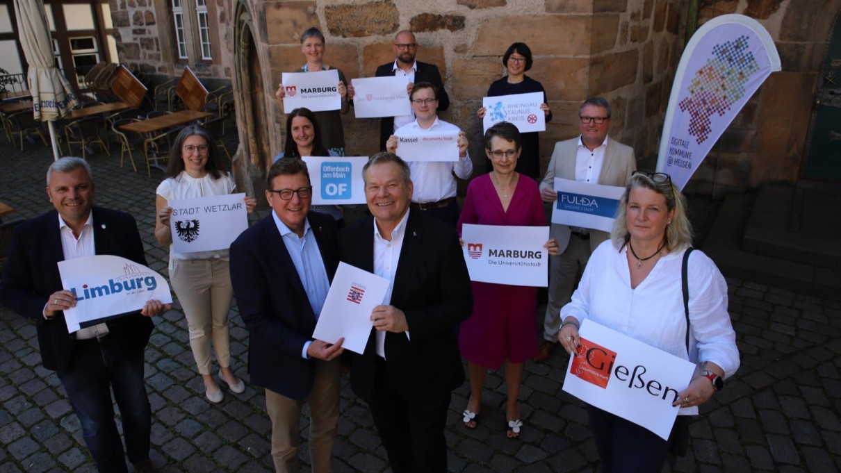 9 Kommunen und landkreise bekommen von Staatsekretär Sauer einen Förderbescheid überreicht. Die Teilnehmende halten Schilder mit den Logo's der 9 Städte und Landkreise hoch. 9 Kommunen und landkreise bekommen von Staatsekretär Sauer einen Förderbescheid überreicht. Die Teilnehmende halten Schilder mit den Logo's der 9 Städte und Landkreise hoch.