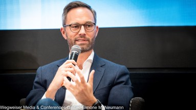 Das Bild zeigt Sascha Soyk, CEO und Gründer von GovRadar. Er hält ein Mikrofon in der Hand. 